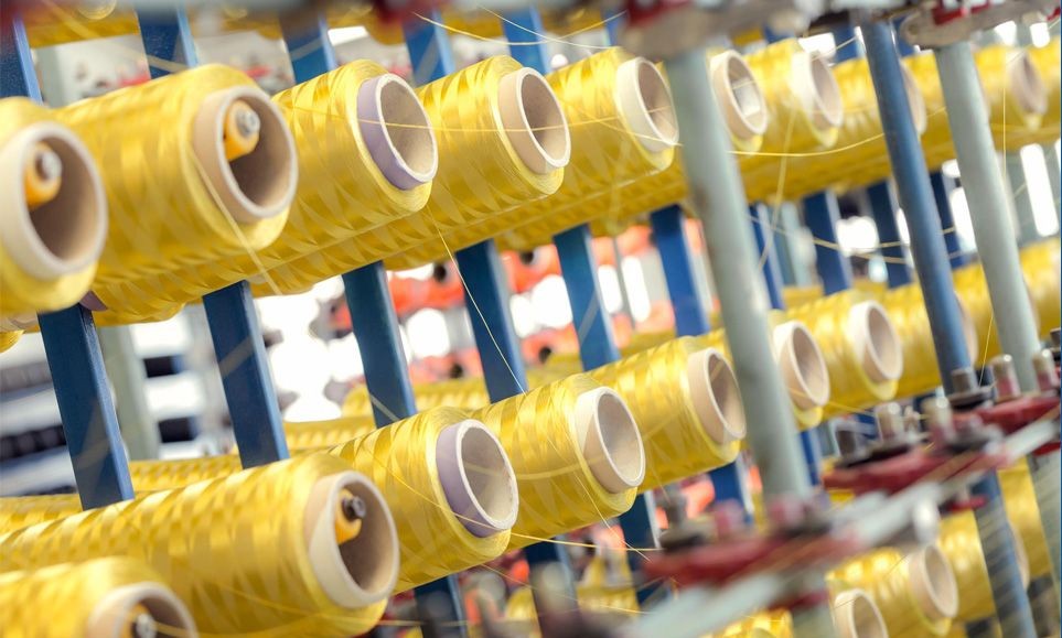 Close-up of yellow spools of thread on a blue metal rack in a textile manufacturing facility.